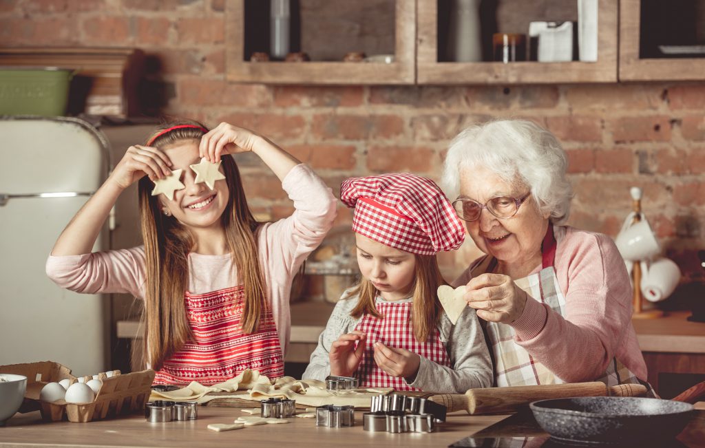 Grandma teaching granddaughters to bake Christmas cut-out cookies.