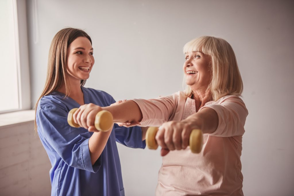 Nurse assists elderly woman with physical therapy using dumbbells