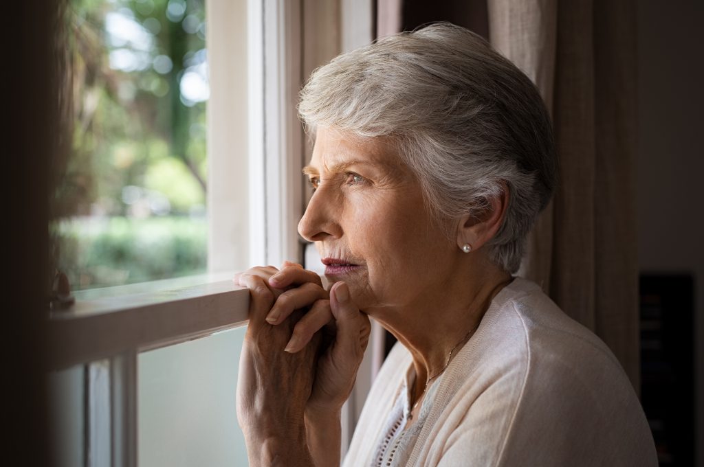 Sad elderly woman looks out the window