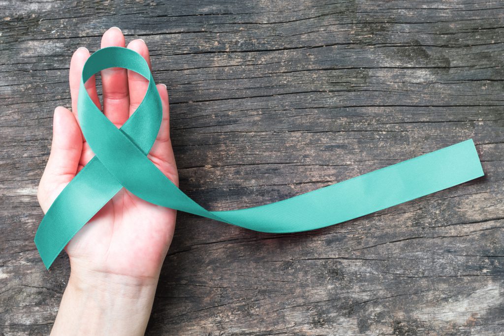 Hand holding a teal ribbon for ovarian cancer awareness