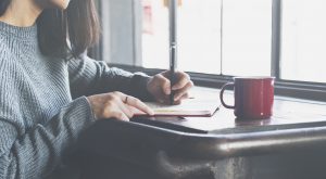 photo of woman writing letter at a table with a red mug